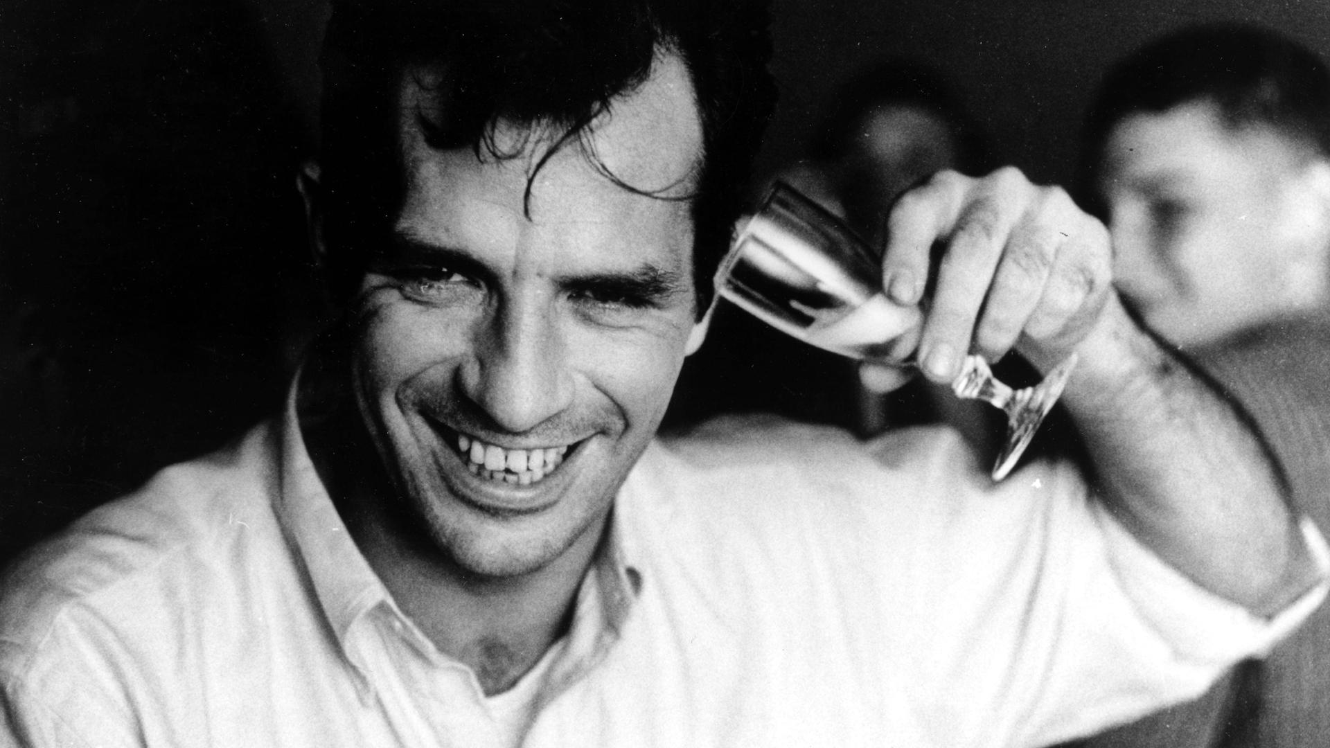 Porträt von Jack Kerouac, der sich lachend ein Sektglas ans Ohr hält. Porträt von Jack Kerouac, der sich lachend ein Sektglas ans Ohr hält.