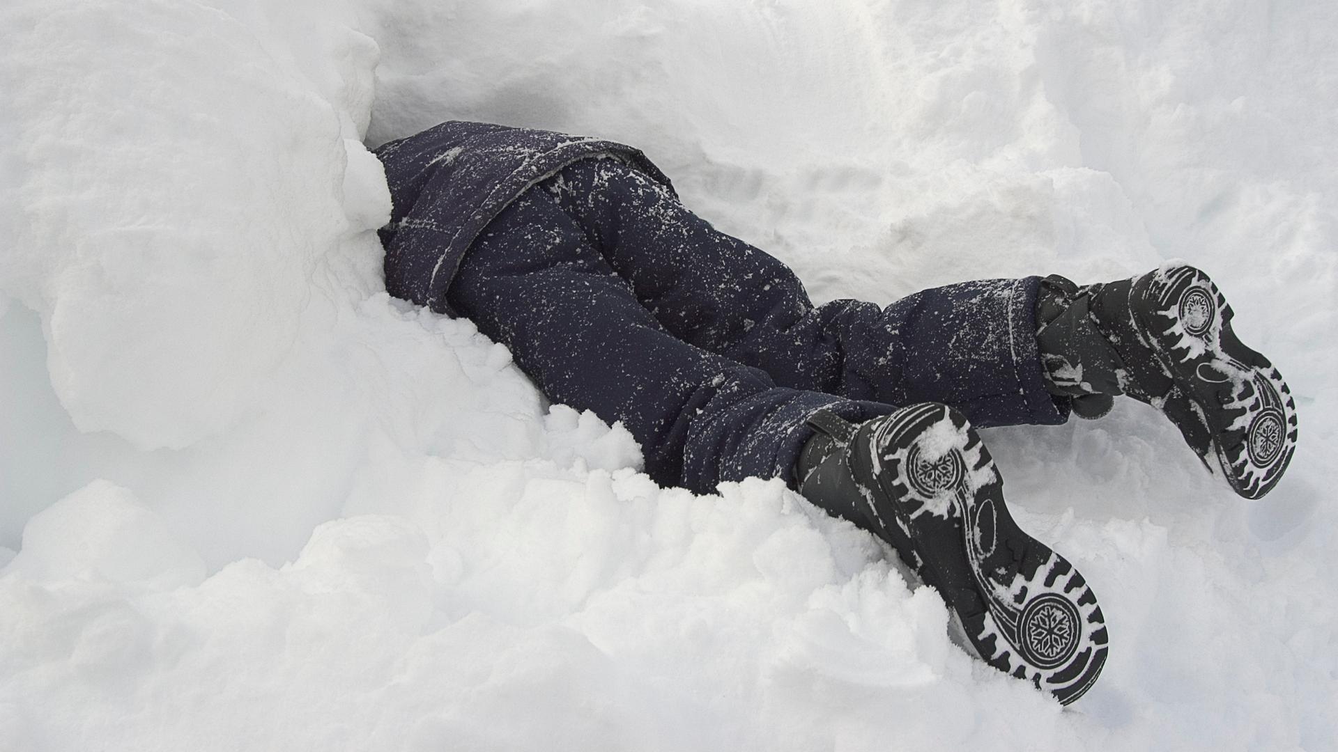 Ein Kind in dunkler Winterkleidung steckt Kopf voran in einem Schneehaufen.
