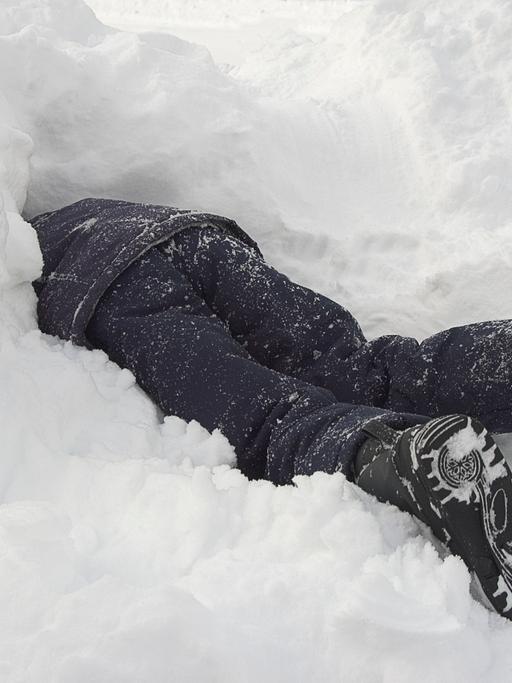 Ein Kind in dunkler Winterkleidung steckt Kopf voran in einem Schneehaufen.
