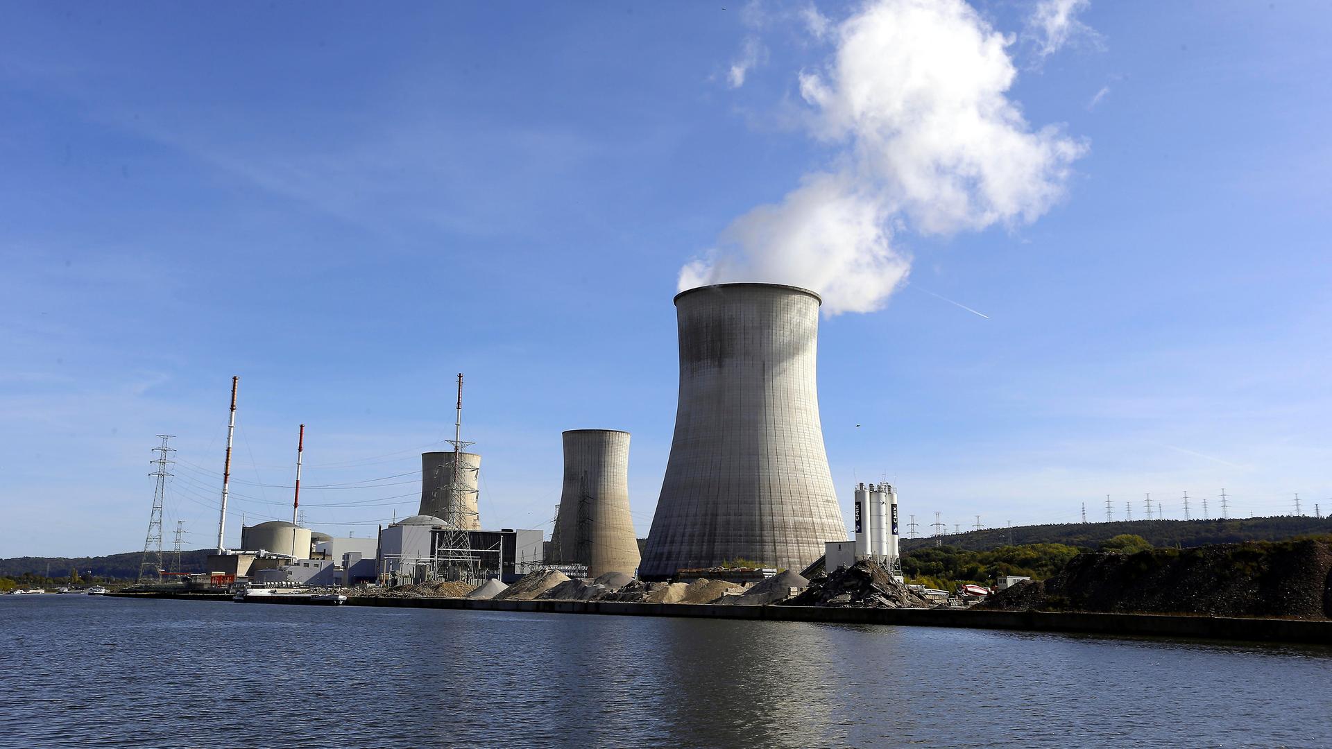 Die drei Kühl-Türme von dem belgischen Atom-Kraft-Werk Tihange stehen am Ufer von dem Fluss Maas. Aus dem rechten Kühl-Turm steigt weißer Dampf in den blauen Himmel.