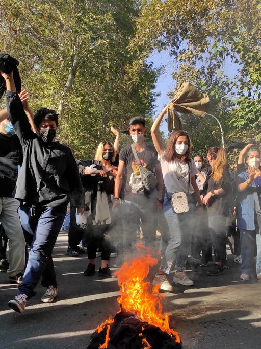 Iranische Demonstranten setzen ihre Schals in Brand, während sie am 1. Oktober 2022 in Teheran eine Straße entlang marschieren. Das Bild wurde mit einer Handykamera aufgenommen. 