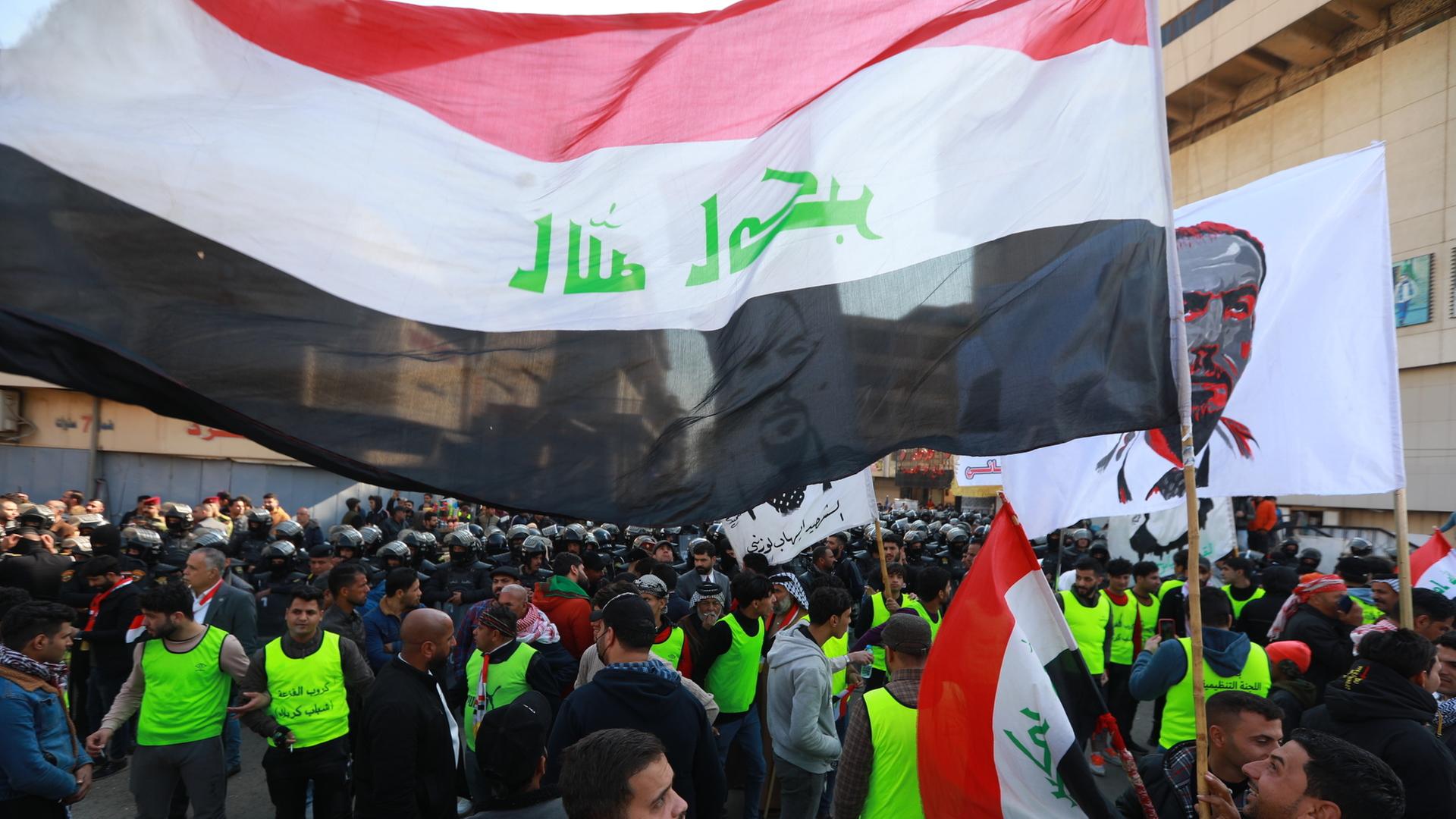 Menschen stehen mit grellen Westen und Fahnen in der Nähe des Zentralbankgebäudes in der irakischen Hauptstadt Baghdad auf der Strasse.