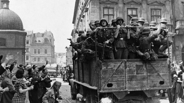 Soldaten der deutschen Wehrmacht fahren am 2. Juli 1941 in einem Militärfahrzeug in die Stadt Lviv, die in der heutigen Ukraine liegt. Am Rand stehen Menschen und jubeln ihnen zu.