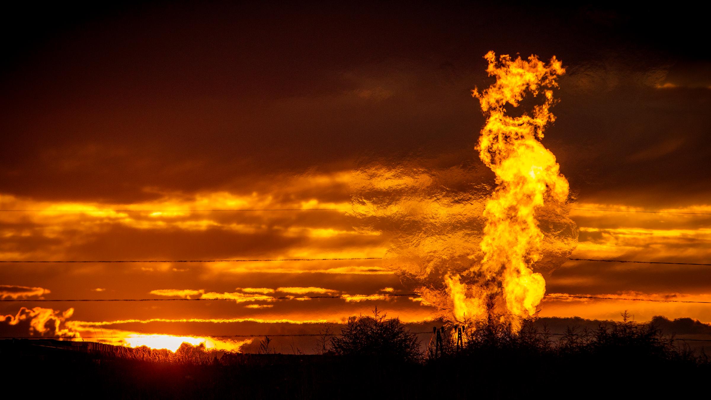 Eine Flamme schlägt vor glutrotem Abendhimmel auf einem Erdgasfeld in die Luft.