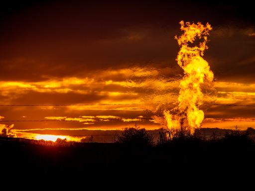 Eine Flamme schlägt vor glutrotem Abendhimmel auf einem Erdgasfeld in die Luft.