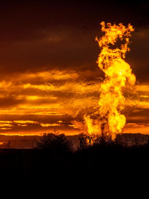 Eine Flamme schlägt vor glutrotem Abendhimmel auf einem Erdgasfeld in die Luft.