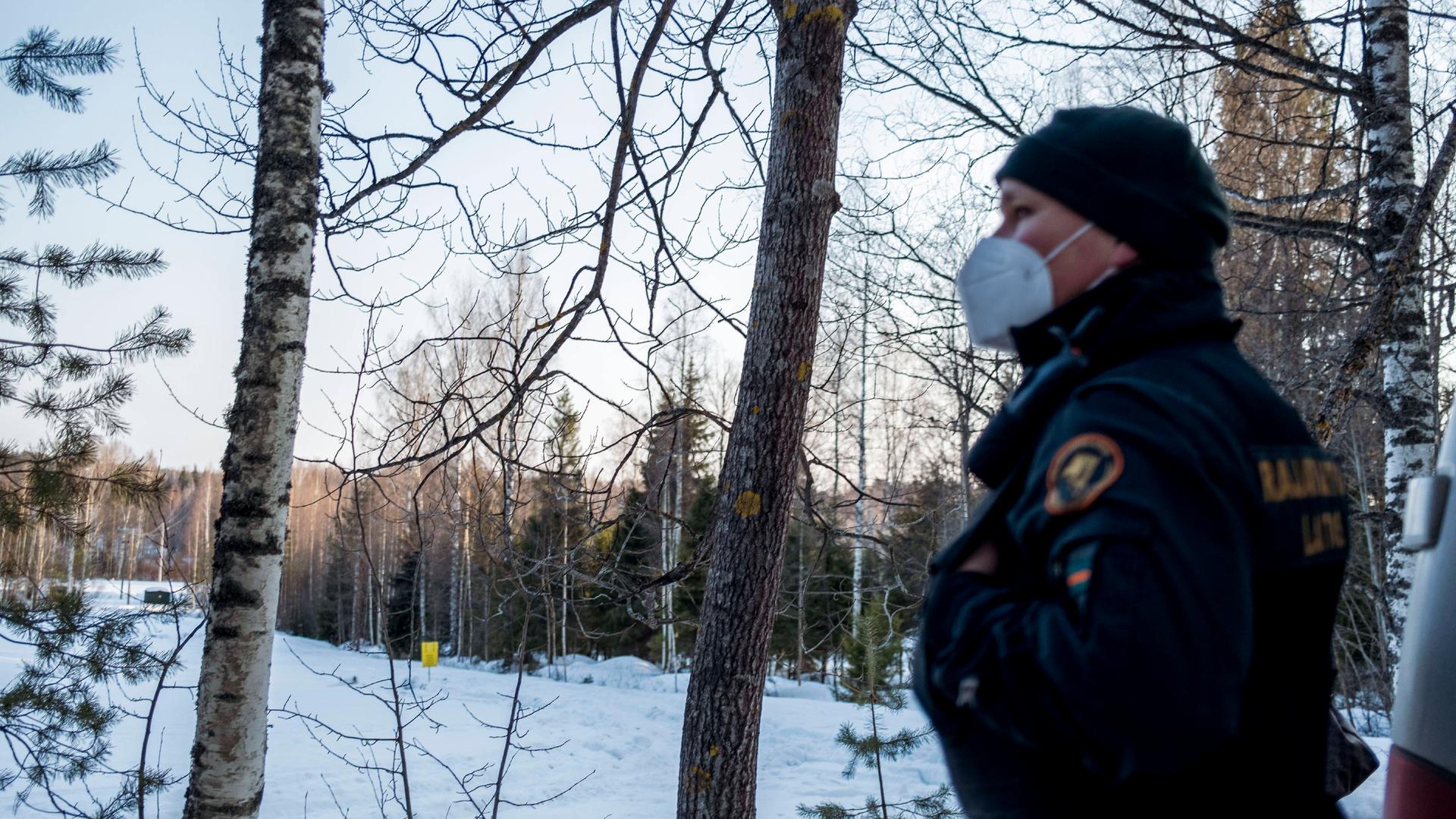 Ein Wachmann mit Mundschutz steht an einer Waldlichtung mit Schnee. Ein Wachmann mit Mundschutz steht an einer Waldlichtung mit Schnee.