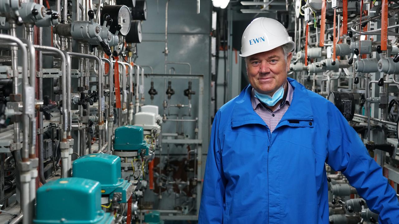 Mann in Blaumann und mit Helm steht in einem Raum mit sehr viel technischen Geräten. Mann in Blaumann und mit Helm steht in einem Raum mit sehr viel technischen Geräten.
