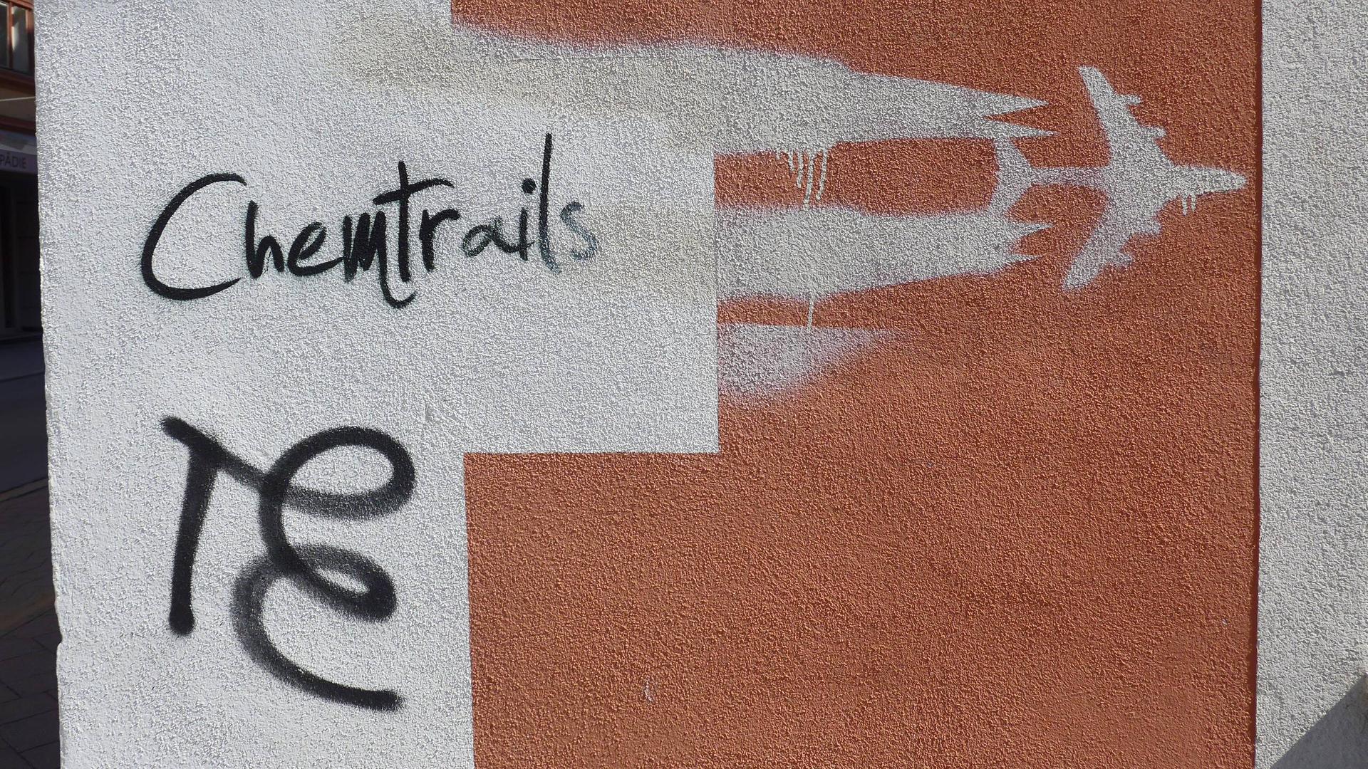 Ein Graffito an einer Hauswand zeigt ein Düsenflugzeug mit Kondensstreifen und den Schriftzug Chemtrails. Ein Graffito an einer Hauswand zeigt ein Düsenflugzeug mit Kondensstreifen und den Schriftzug Chemtrails.