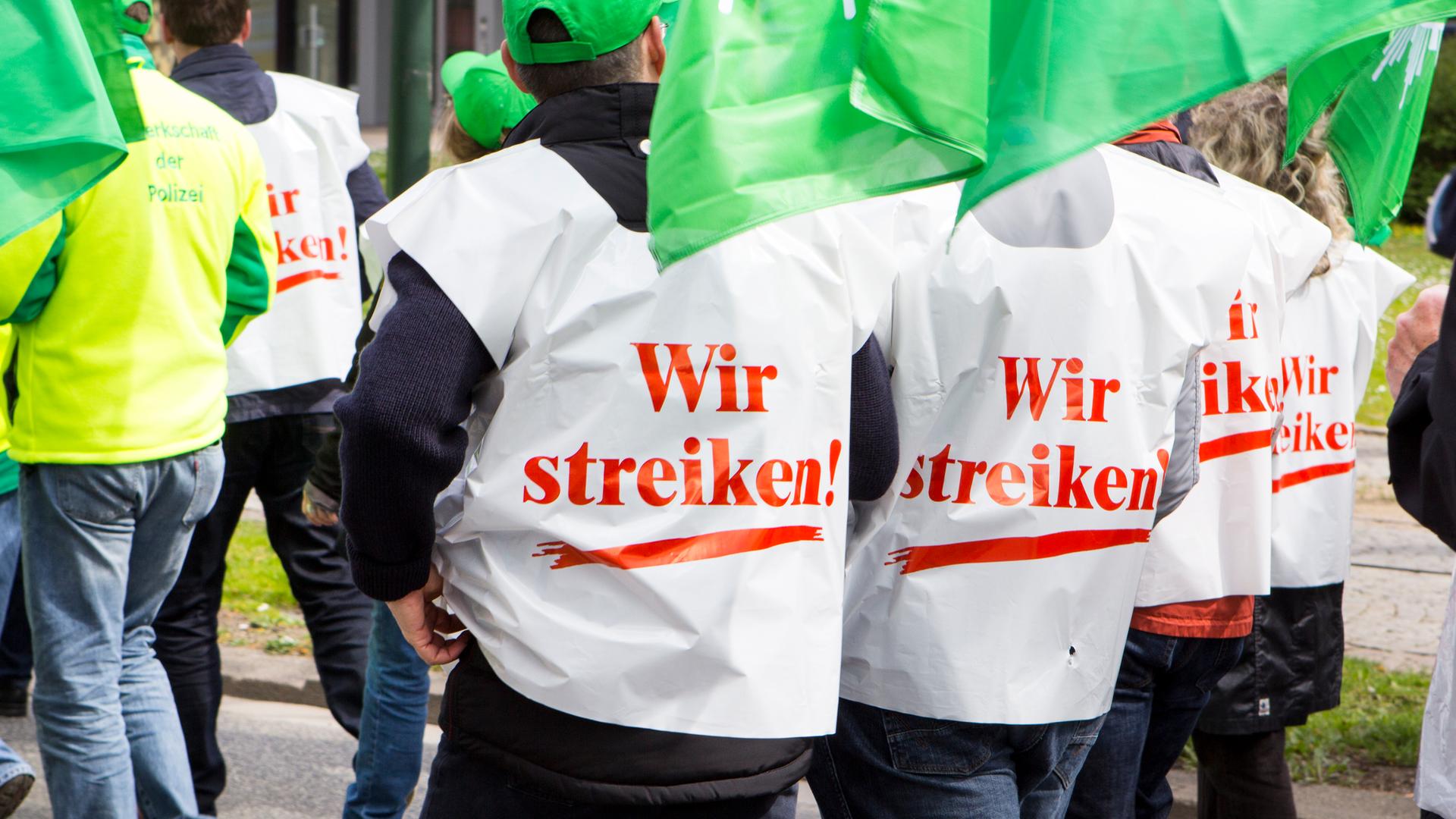 Personen mit Westen auf denen "Wir streiken" steht demonstrieren für Lohnerhöhungen.