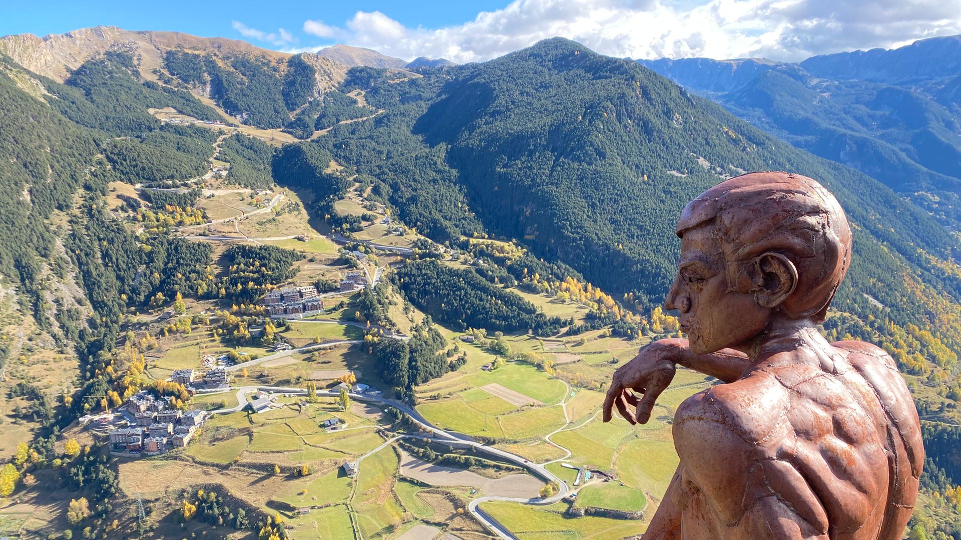 Von einer Aussichtsplattform aus betrachtet eine Statue sitzend das Bergpanorama der Pyrenäen.