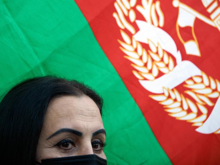 Eine Frau mit halbverschleiertem Gesicht, hinter ihr ist die afghanische Flagge zu sehen. 