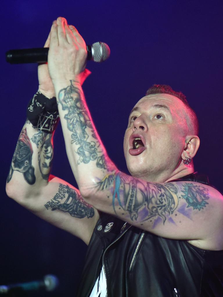 Der Sänger der Punkrockband Tarakany! singt auf einer Bühne. Er hebt seine tätowierten Arme, die das Mikrofon halten.