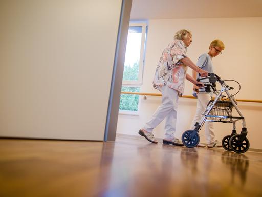 Debatte über Fachkräftemangel in der Pflege: Eine Pflegekraft geht in einem Pflegeheim mit einer älteren Dame über einen Korridor