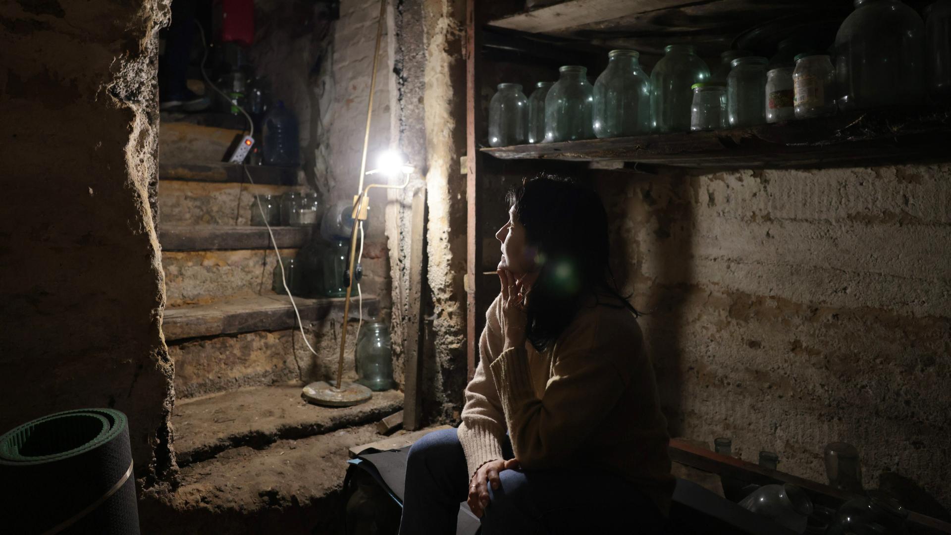 Krieg in der Ukraine. Eine Frau sitzt in ihrem Keller im Schein einer kleinen Lampe und wartet auf das Ende der Kämpfe. Avdeyevka, Ukraine, 2022.