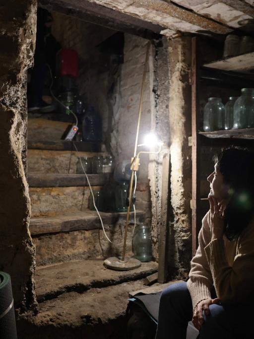 Krieg in der Ukraine. Eine Frau sitzt in ihrem Keller im Schein einer kleinen Lampe und wartet auf das Ende der Kämpfe. Avdeyevka, Ukraine, 2022.