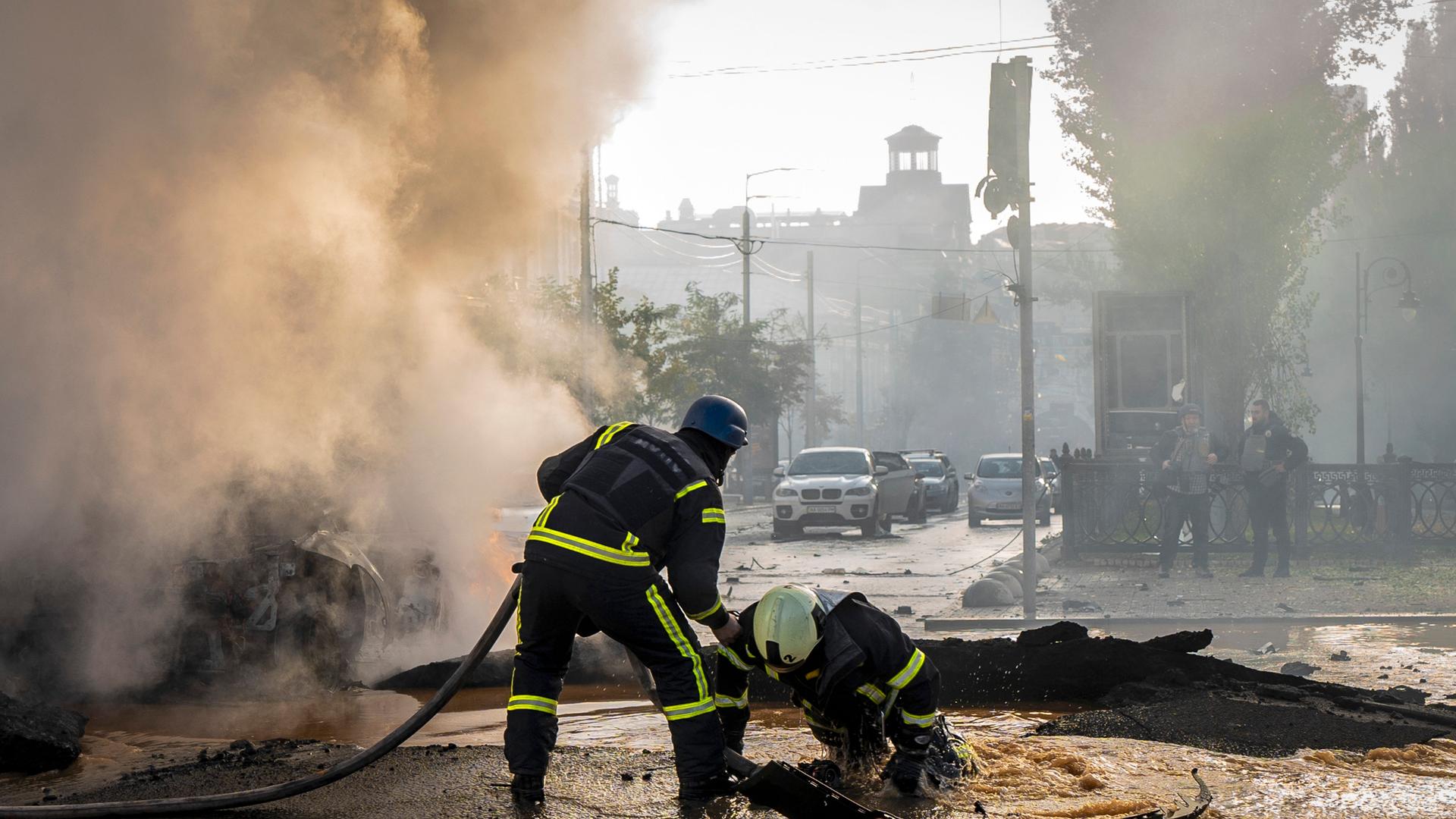 Ein Feuerwehr-Mann hilft seinem Kollegen aus einem mit Wasser gefüllten Krater. Ein Feuerwehr-Mann hilft seinem Kollegen aus einem mit Wasser gefüllten Krater.