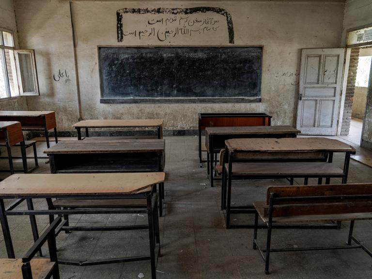 Ein leeres Klassenzimmer mit Blick auf eine Tafel an der Wand und Holztischen und Sitzen in einer Mädchenschule, die von den Taliban geschlossen wurde.