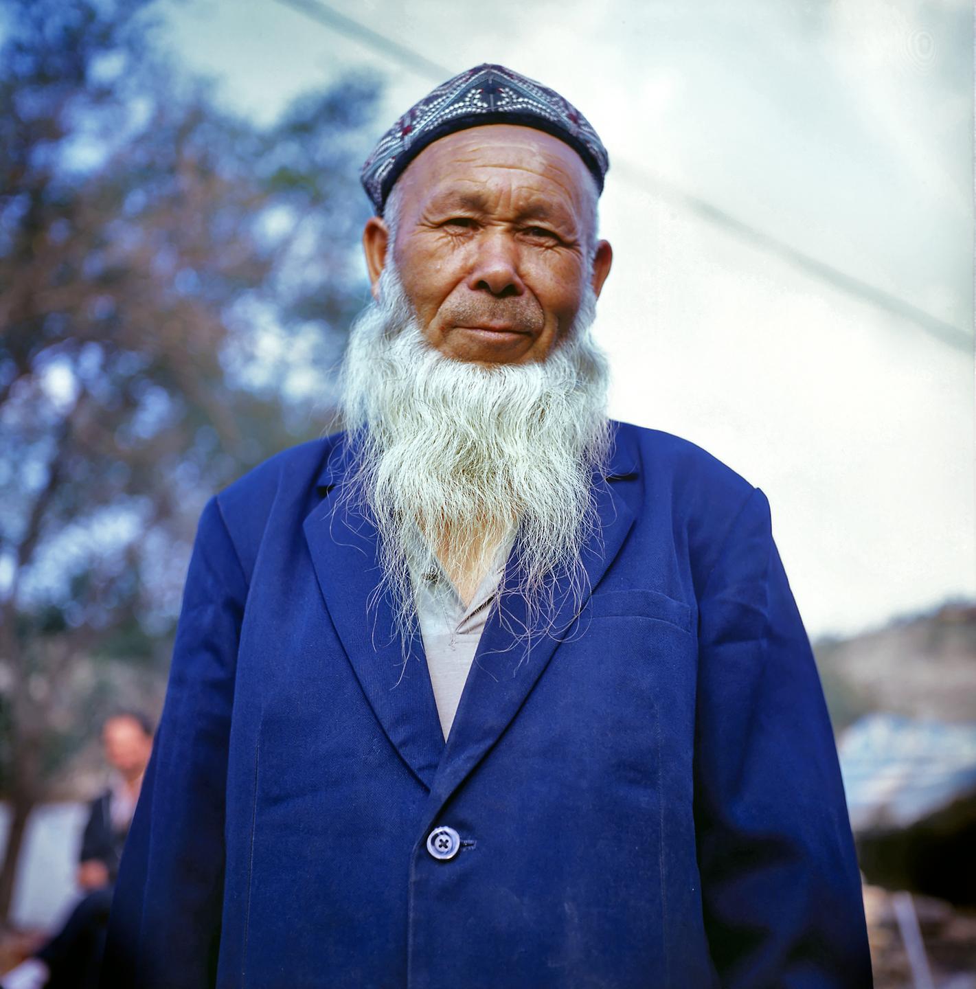 Porträt eines älteren Uiguren mit einem langen, weißen Bart und einer bestickten Kopfbedeckung.