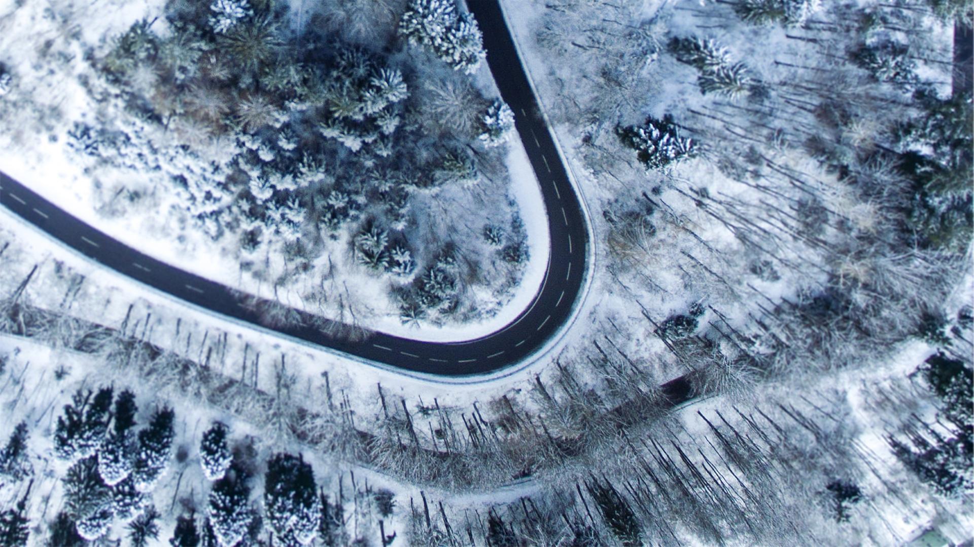 Eine sich schlängelnde Straße in verschneiter Waldlandschaft aus der Vogelperspektive. Eine sich schlängelnde Straße in verschneiter Waldlandschaft aus der Vogelperspektive.