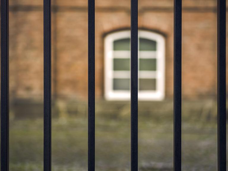 Blick durch ein Gitter auf einen Gefängnishof.