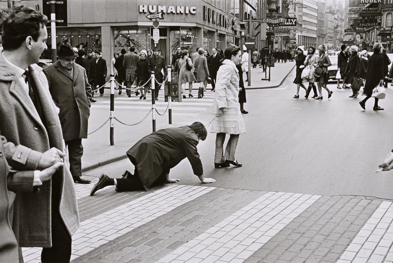 Schwarz-weiß-Foto von der Künstlerin Valie Export, die den Künstler Peter Weibel an einer Leine über einen Zebrastreifen in der Wiener Innenstadt führt. Schwarz-weiß-Foto von der Künstlerin Valie Export, die den Künstler Peter Weibel an einer Leine über einen Zebrastreifen in der Wiener Innenstadt führt.