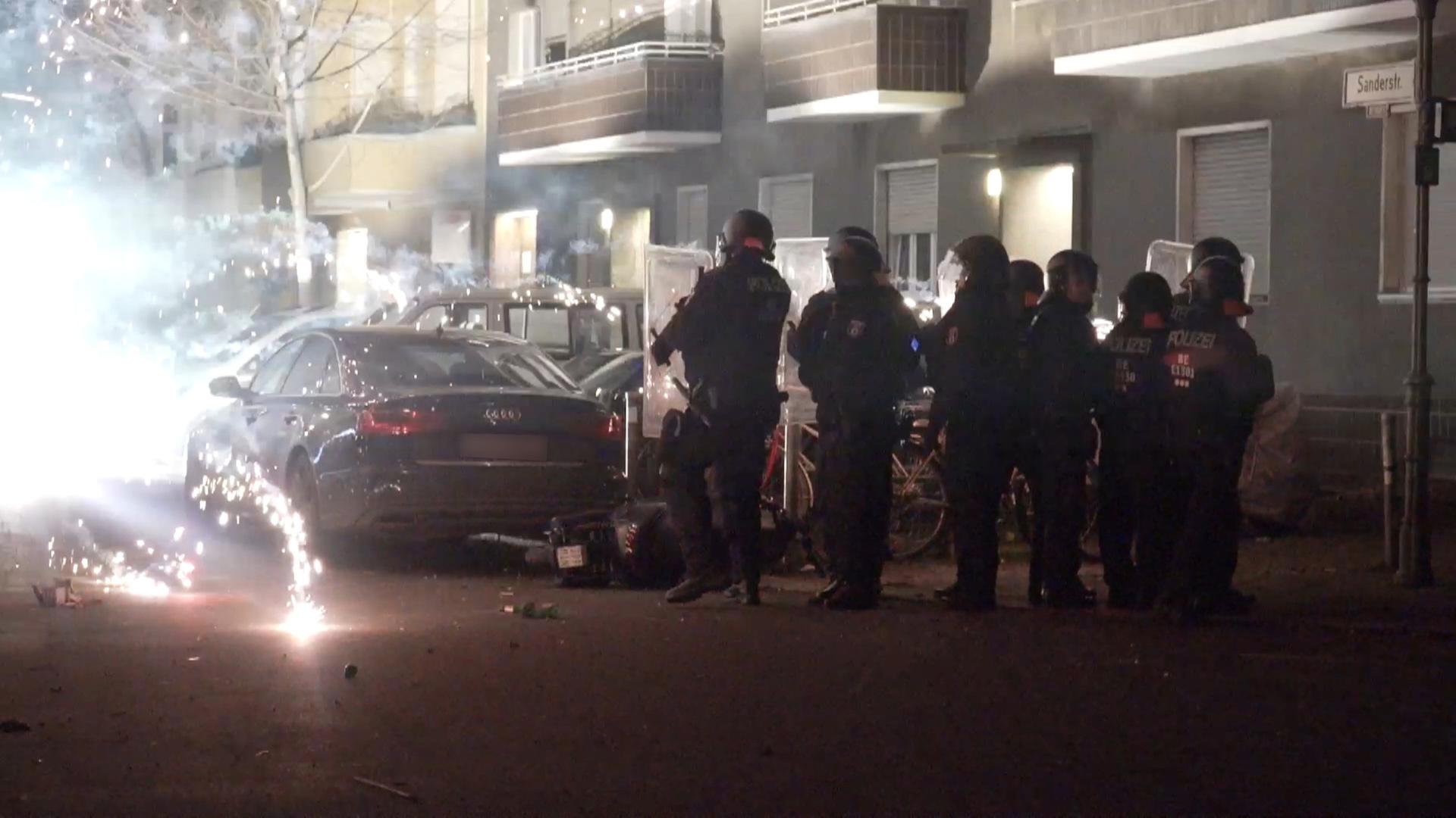 Polizeibeamte stehen hinter explodierendem Feuerwerk.. Berlins Regierende Bürgermeisterin will, dass sich die Innenminister mit dem Thema beschäftigen.