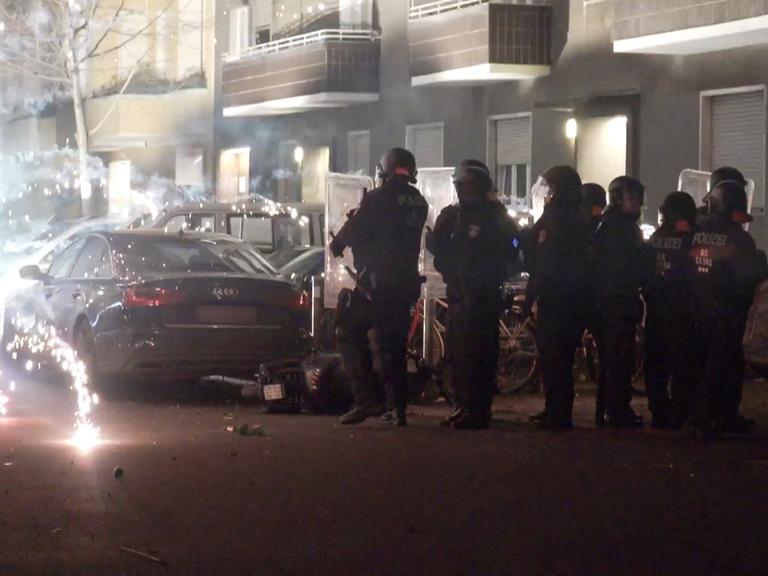 Polizeibeamte stehen hinter explodierendem Feuerwerk.. Berlins Regierende Bürgermeisterin will, dass sich die Innenminister mit dem Thema beschäftigen.