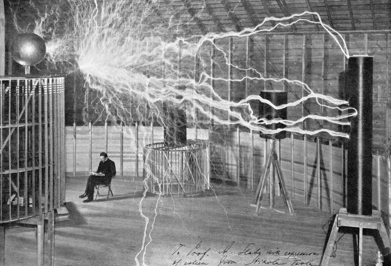 Tesla in seinem Labor in Colorado Springs im Dezember 1899. Die Aufnahme stellt eine Mehrfachbelichtung dar: Während der Blitzentladungen befand sich Tesla nicht im Raum. Tesla in seinem Labor in Colorado Springs im Dezember 1899. Die Aufnahme stellt eine Mehrfachbelichtung dar: Während der Blitzentladungen befand sich Tesla nicht im Raum.