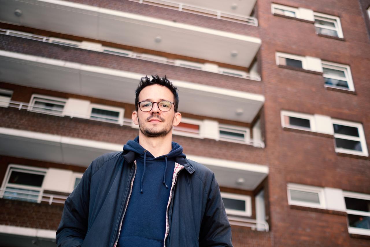 Der Autor Olivier David vor einem mehrgeschossigen Haus aus der Froschperspektive. Der Autor Olivier David vor einem mehrgeschossigen Haus aus der Froschperspektive.