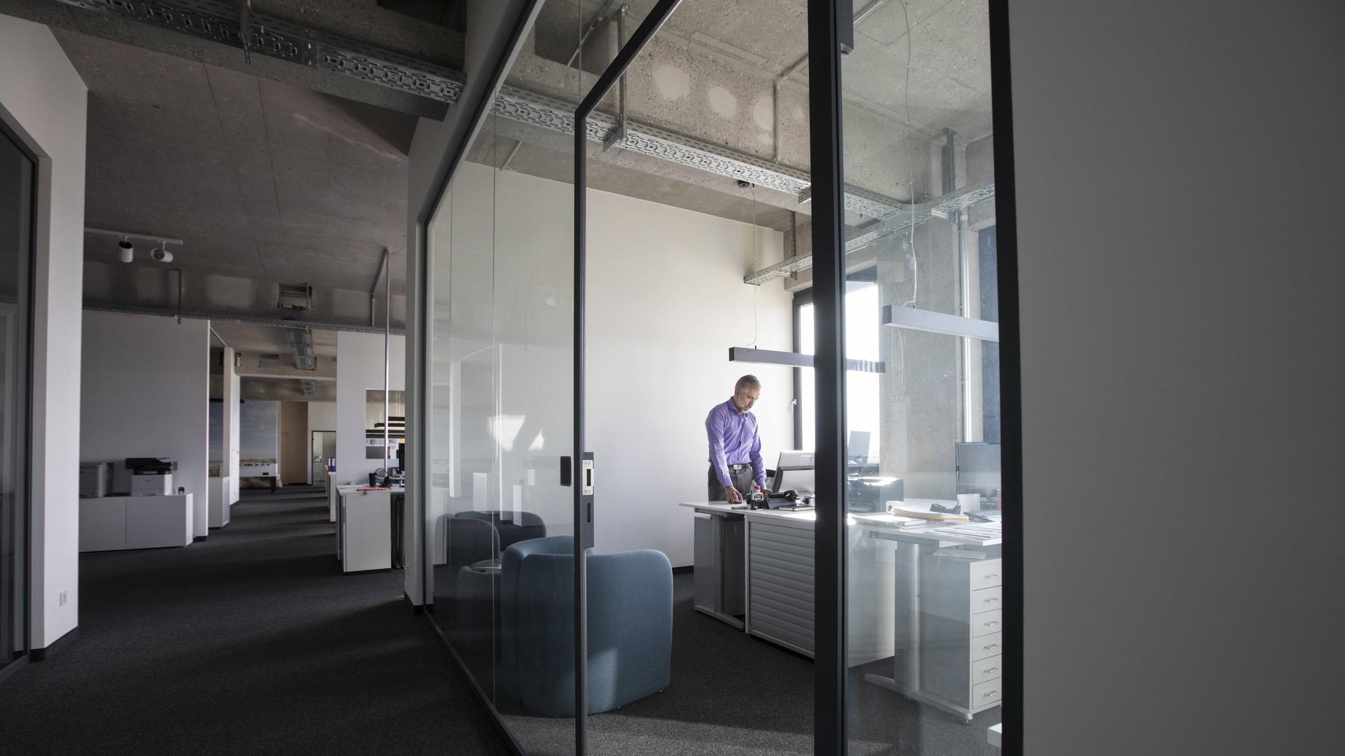 Ein Geschäftsmann allein in einem Büro mit Glastüren auf einer Büroetage Ein Geschäftsmann allein in einem Büro mit Glastüren auf einer Büroetage