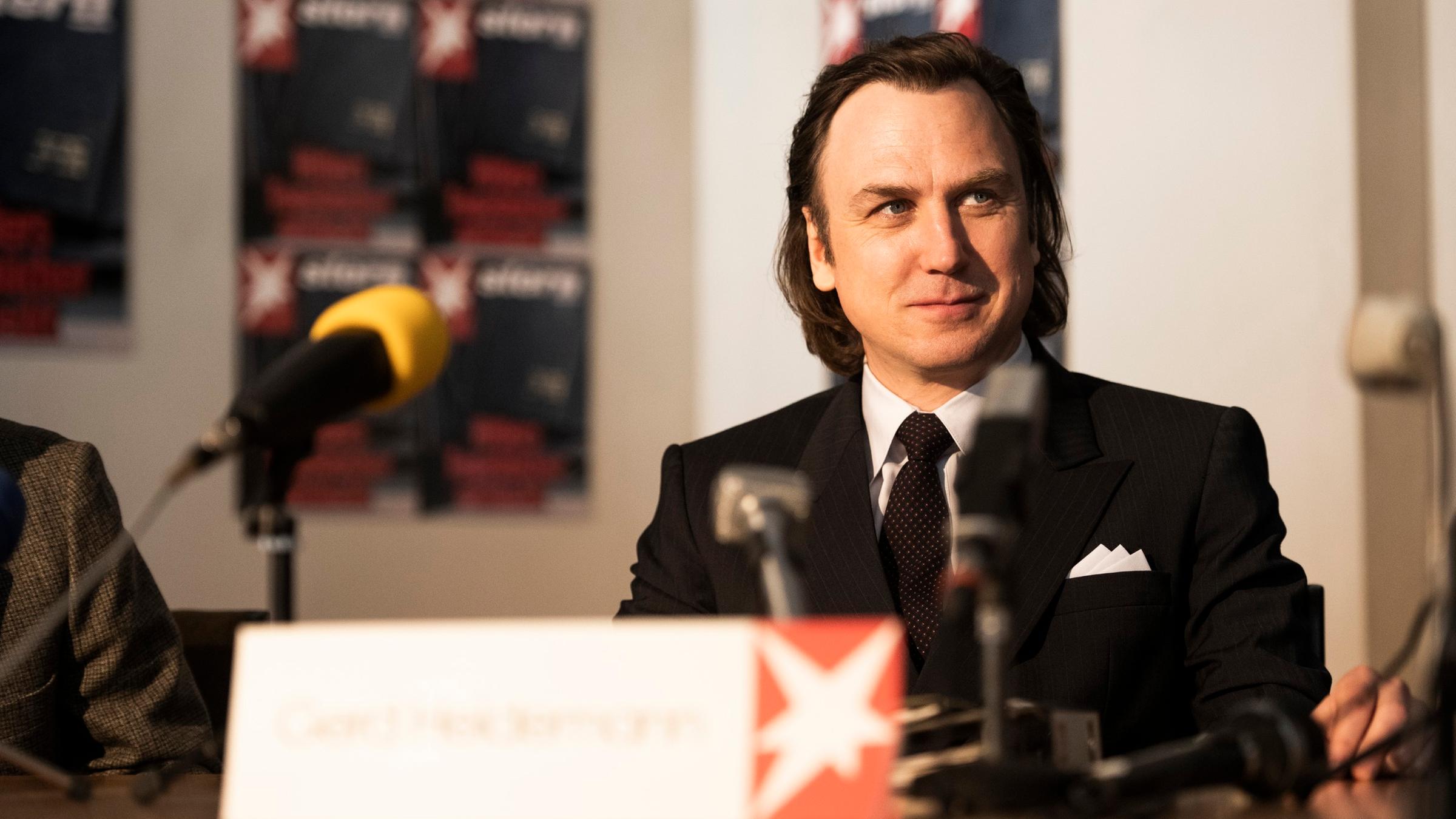 Schauspieler Lars Eidinger sitzt in seiner Figur des Reporters Gerd Heidemann in "Faking Hitler" bei einer Presskonferenz. Schauspieler Lars Eidinger sitzt in seiner Figur des Reporters Gerd Heidemann in "Faking Hitler" bei einer Presskonferenz.