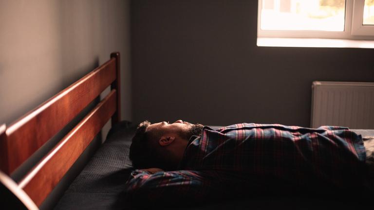 Ein Mann liegt auf einem Bett und schaut aus dem Fesnter Ein Mann liegt auf einem Bett und schaut aus dem Fesnter