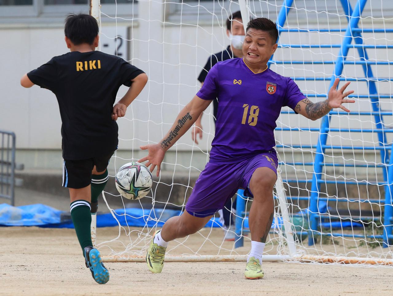 サッカーの元ミャンマー代表ゴールキーパー、ピャエ・リャン・アウンさんは、子供たちとサッカーの試合中に少年の写真を持っている。 