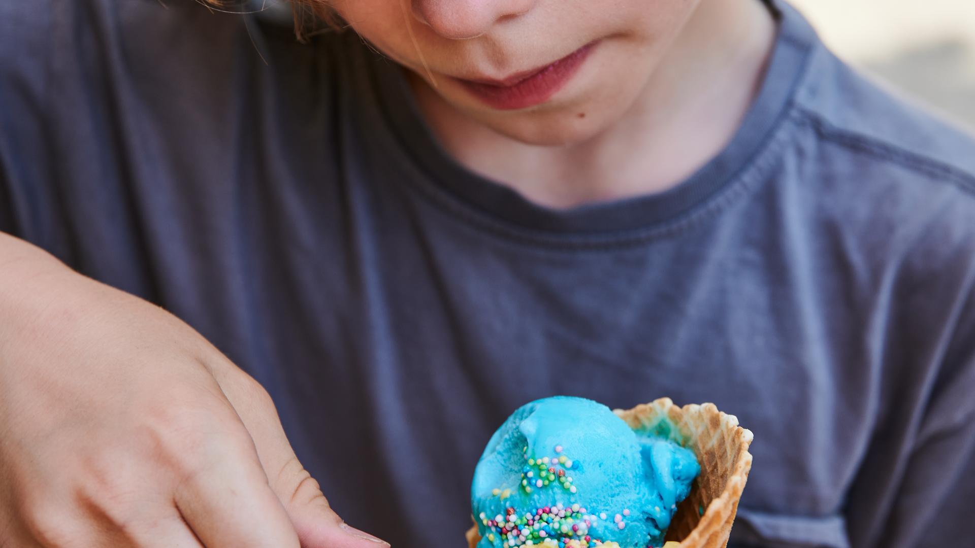 Ein Kind isst buntes Eis mit unterschiedlichen Geschmacksrichtungen aus der Waffel.