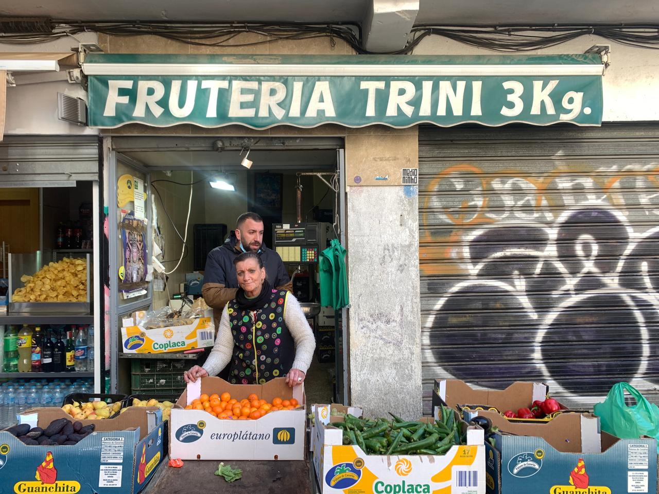 Ein Frau in buntem Kittel steht an einem Markstand vor eine Kiste voller Orangen. Um sie herum viele Kisten mit Gemüse. Ein Frau in buntem Kittel steht an einem Markstand vor eine Kiste voller Orangen. Um sie herum viele Kisten mit Gemüse.