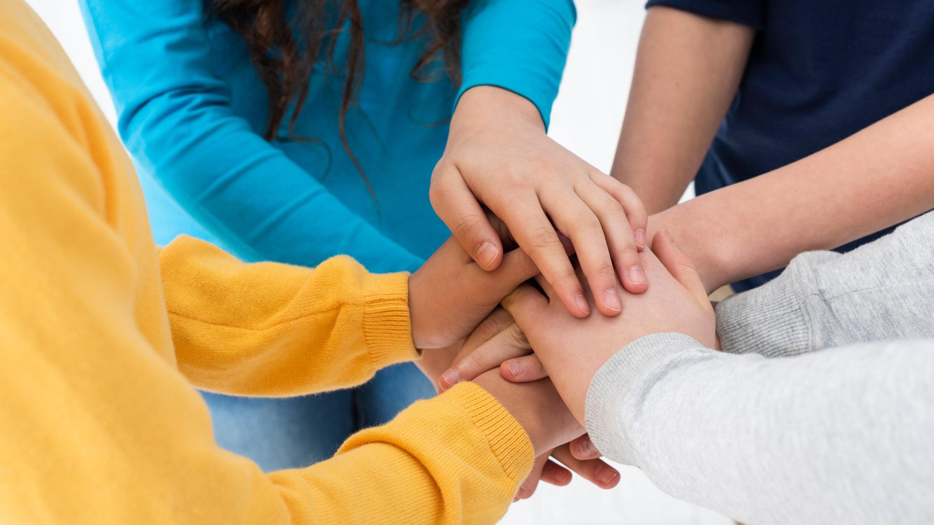 Vier junge Menschen in verschiedenfarbiger Kleidung legen ihre Hände im Kreis übereinander.