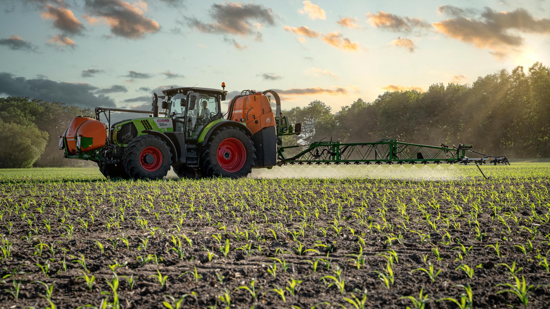 Ein Traktor bringt Pflanzenschutzmittel auf einem Maisfeld aus Ein Traktor bringt Pflanzenschutzmittel auf einem Maisfeld aus
