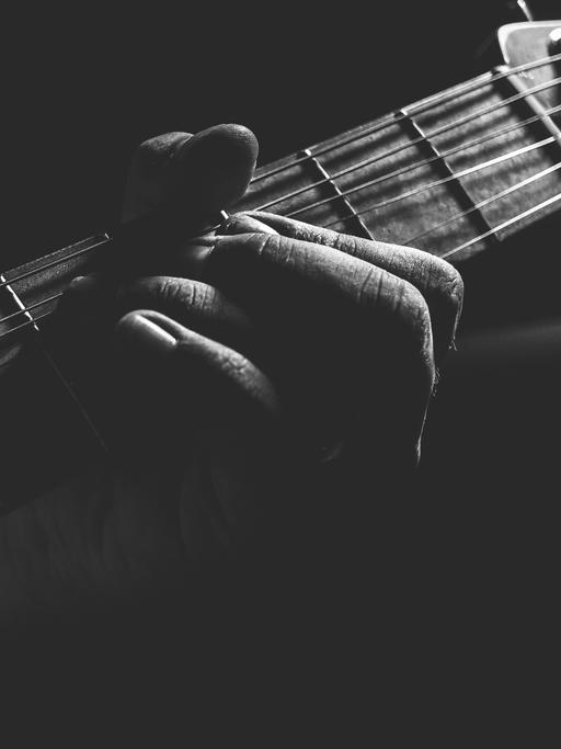 Wir sehen die Nahaufnahme eines Gitarrenhalses, der von Fingern bearbeitet wird.