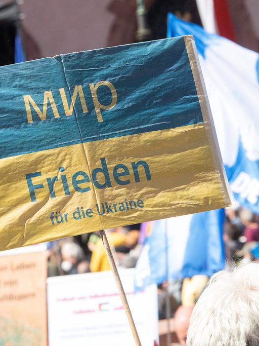 «Frieden für die Ukraine» steht während der Abschlusskundgebung der Ostermärsche des «Netzwerks Friedenskooperative» in Frankfurt und Umgebung auf einem Schild. Im Hintergrund ist eine Fahne mit Friedenstaube zu sehen. 