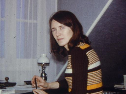 Im Filmstill aus "Annie Ernaux - Die Super-8-Jahre" sitzt Annie Ernaux als junge Frau mit schulterlangem braunem Haar und im Ringelpullover an einem Schreibtisch.