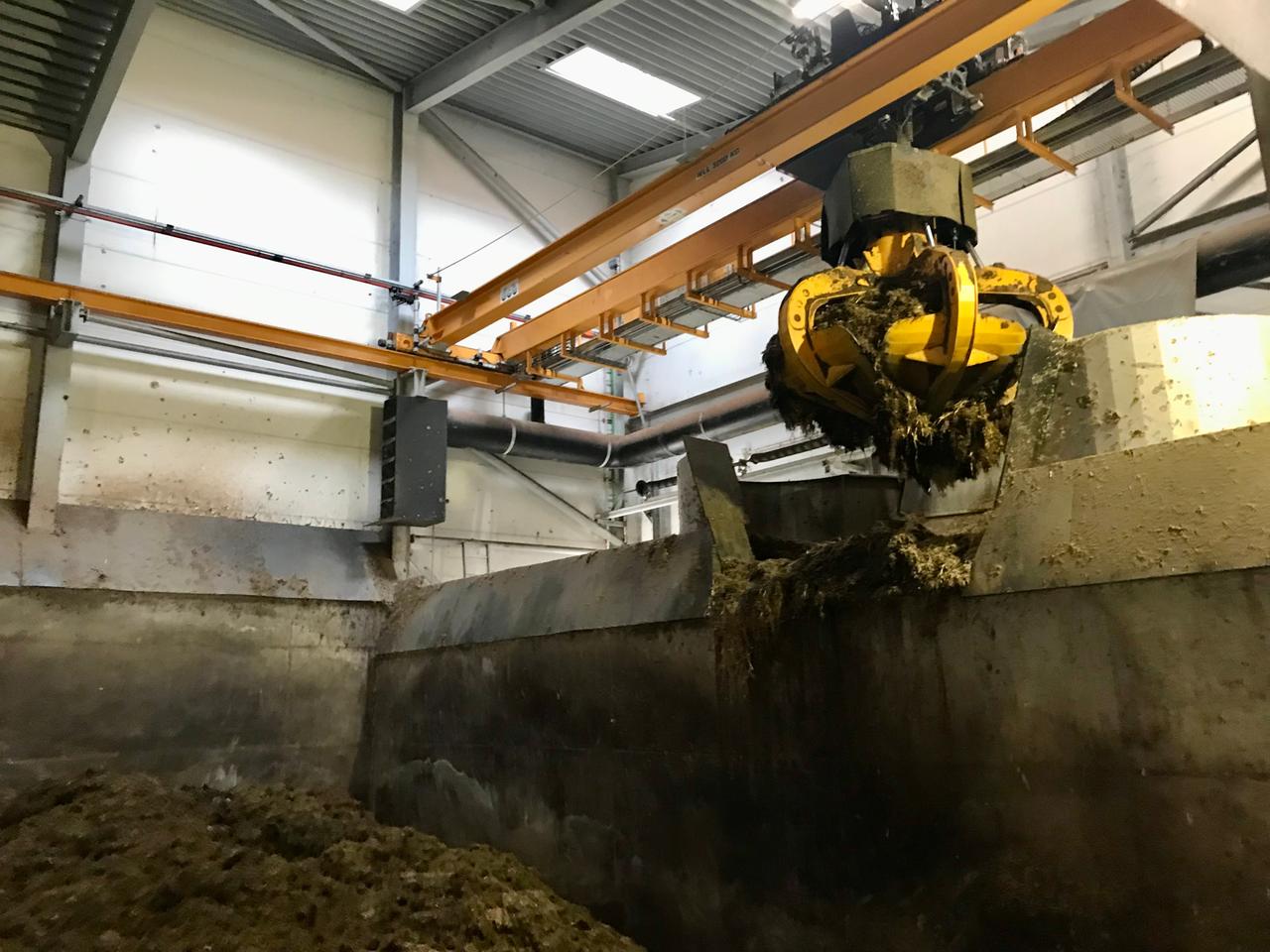 Ein Greifarm transprotiert eine braune Masse in eine Art Container. Ein Greifarm transprotiert eine braune Masse in eine Art Container.