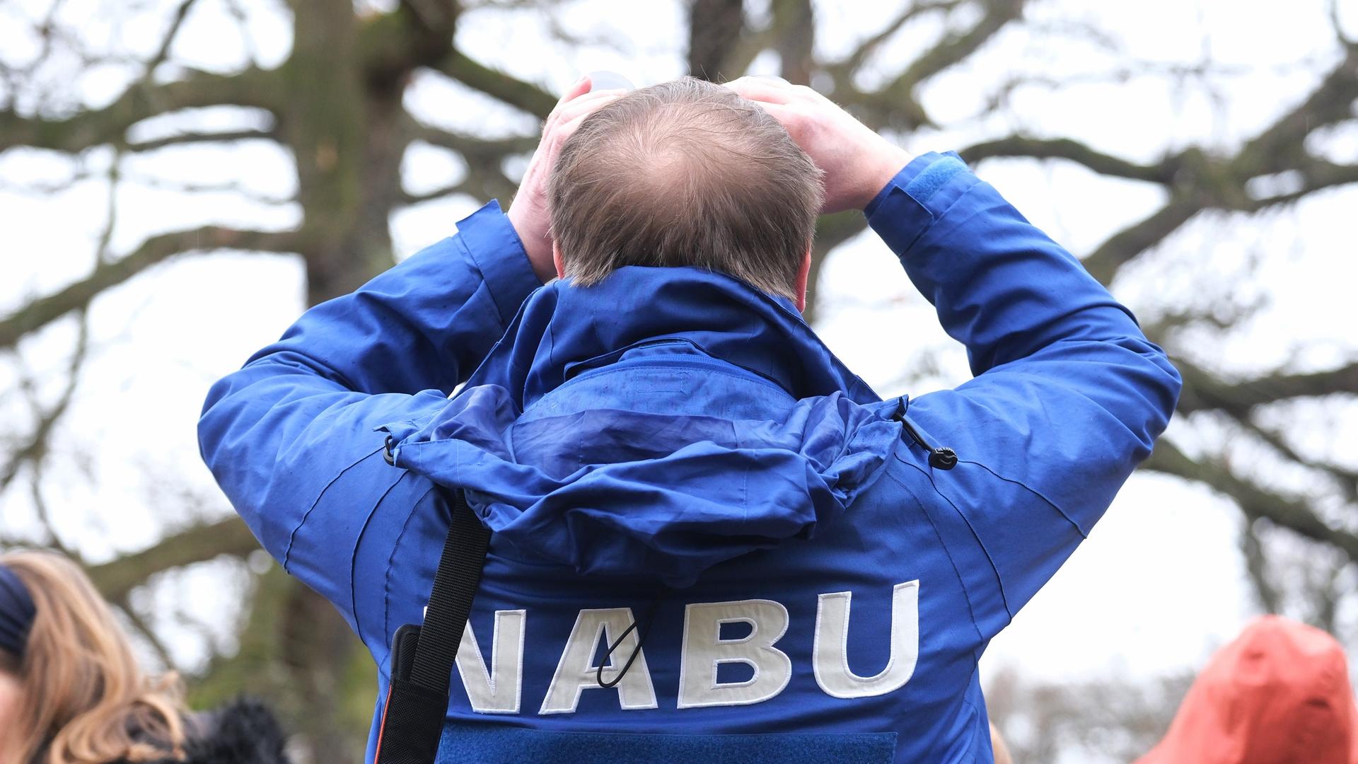 Das Foto zeigt einen Mann mit blauer Jacke und der Aufschrift Nabu. Er steht mit dem Rückem zum Betrachter und blickt durch ein Fernglas, um Vögel zu beobachten. Das Foto zeigt einen Mann mit blauer Jacke und der Aufschrift Nabu. Er steht mit dem Rückem zum Betrachter und blickt durch ein Fernglas, um Vögel zu beobachten.