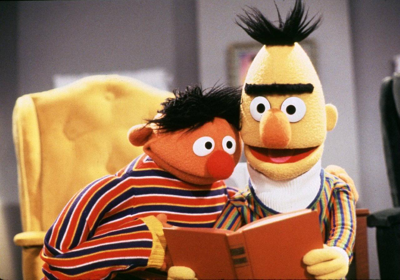  Ernie und Bert aus der Sesamstraße sitzen in einem Sessel und lesen ein Buch.