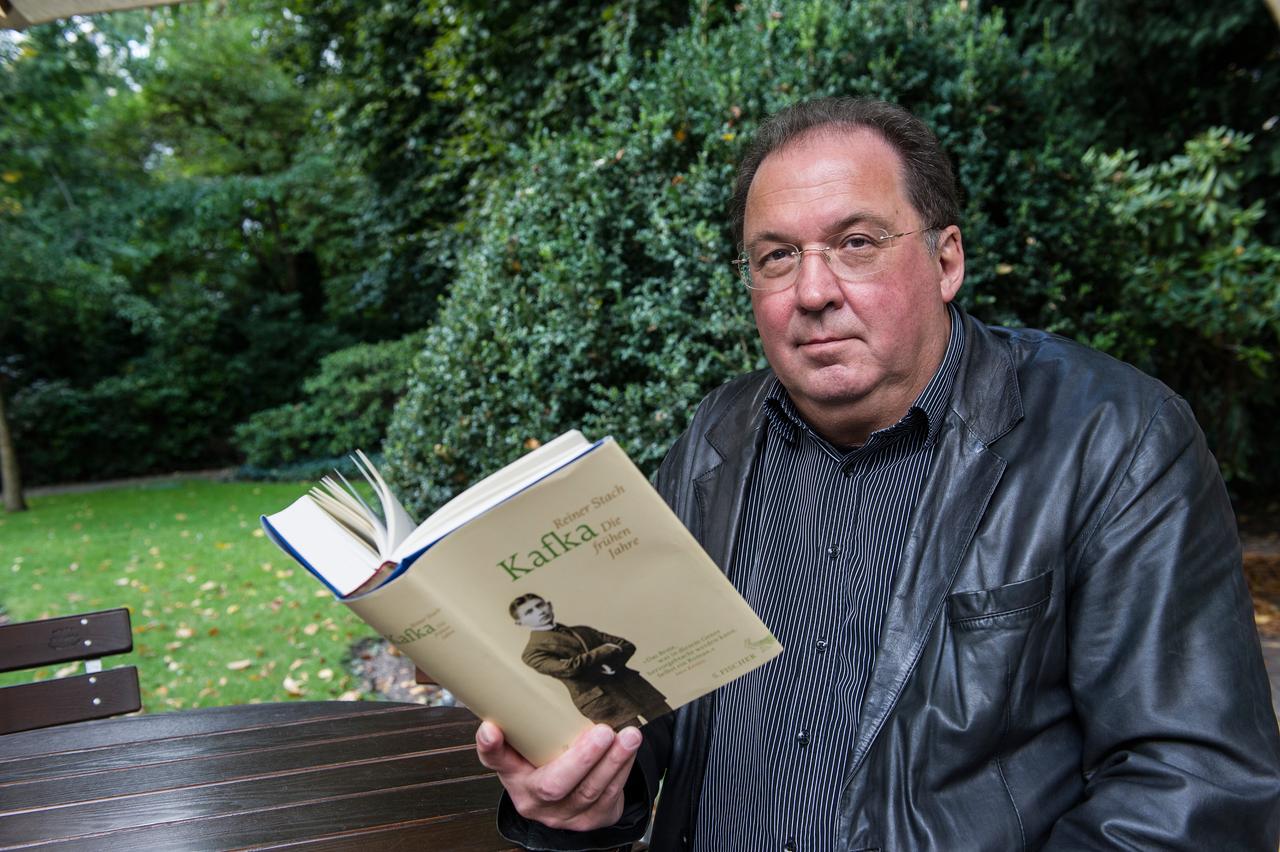 Der Berliner Autor Reiner Stach sitzt in Berlin in einem Garten - in der Hand ein Exemplar seiner Kafka-Biografie.