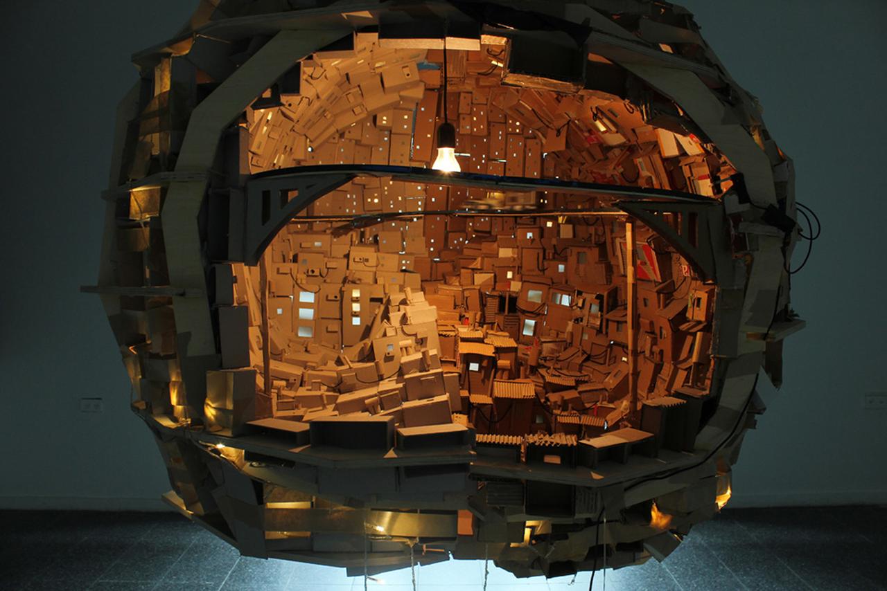 Ein künstlerisches Holzmodell eines Gehirns, das wie eine Stadt aussieht und in dem eine Glühbirne leuchtet.
