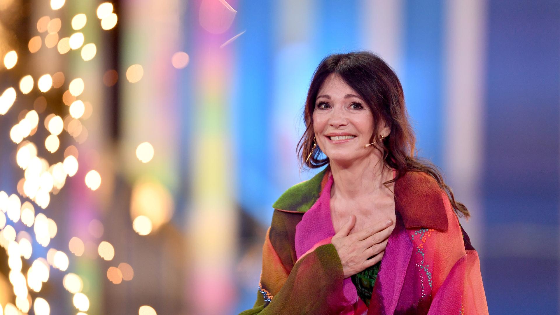 Schauspielerin Iris Berben trägt ein buntes Kleid. Sie legt eine Hand ans Herz und lacht froh in die Kamera. Schauspielerin Iris Berben trägt ein buntes Kleid. Sie legt eine Hand ans Herz und lacht froh in die Kamera.