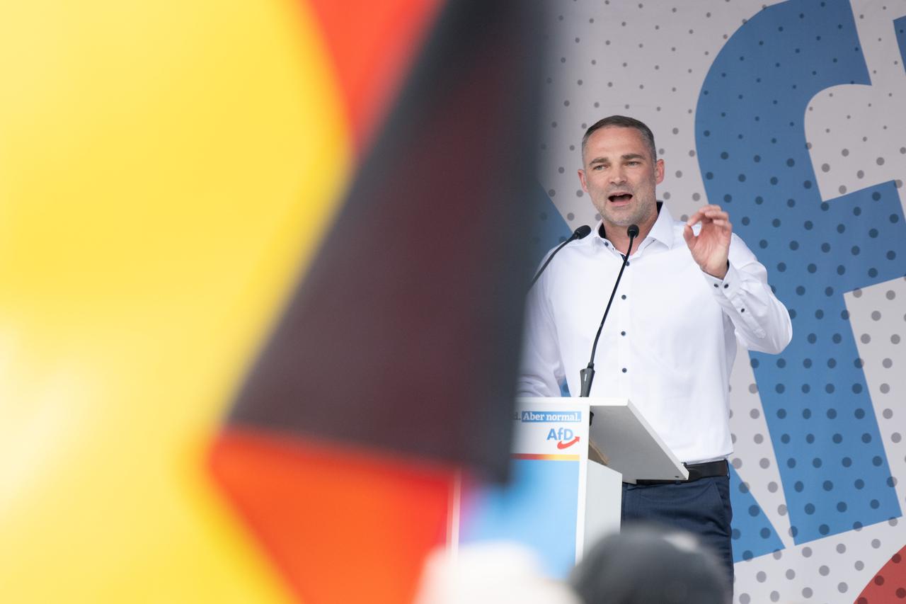 Der AfD-Kandidat für das Amt des Landrats im Landkreis Görlitz, Sebastian Wippel, redet auf einer Bühne. Vor der Kameralinse ist unscharf eine Deutschlandfahne zu sehen, die rund das halbe Bild einnimmt. Der AfD-Kandidat für das Amt des Landrats im Landkreis Görlitz, Sebastian Wippel, redet auf einer Bühne. Vor der Kameralinse ist unscharf eine Deutschlandfahne zu sehen, die rund das halbe Bild einnimmt.