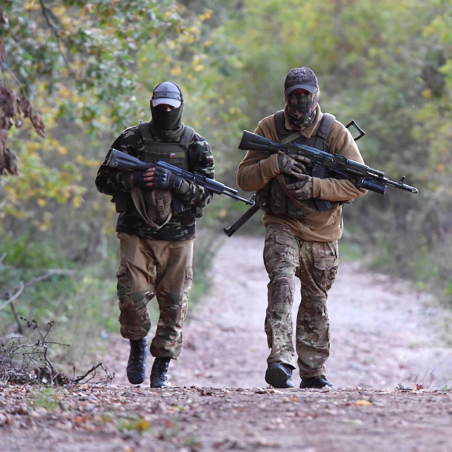 Zwei Mitglieder der russischen Söldnergruppe "Wagner" laufen mit Gewehren durch einen Wald
