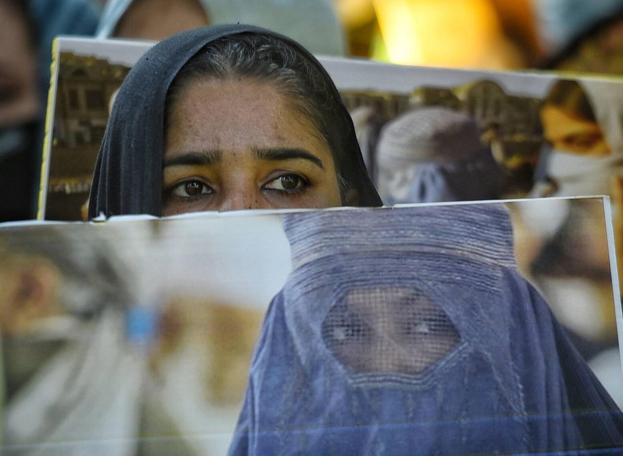 Eine Frau mit Kopftuch hält ein Plakat mit einer Frau in Burka empor.